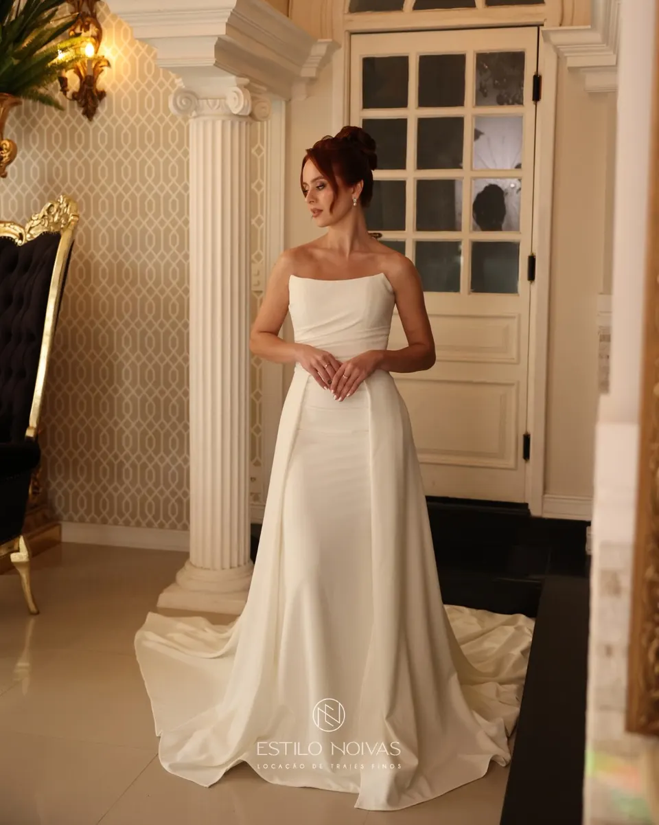 Noiva com vestido de cetim liso e cauda, entre colunas brancas