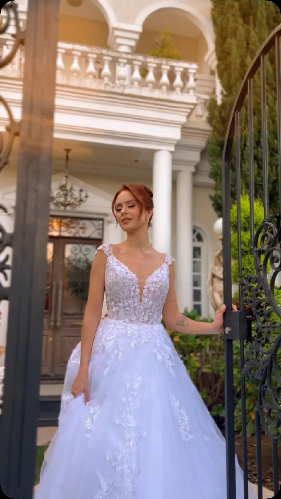 Noiva sorrindo com vestido de corpete rendado diante de porta antiga